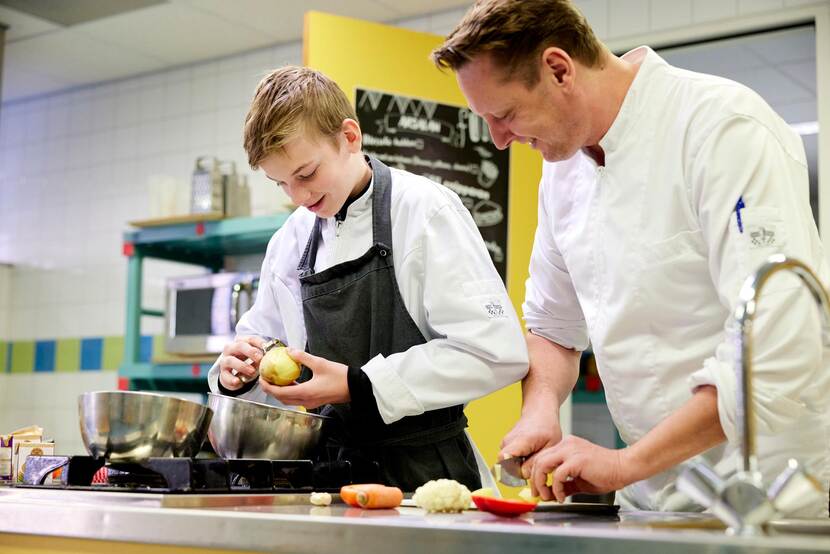 Een leerling schilt aardappelen in de keuken samen met de leraar