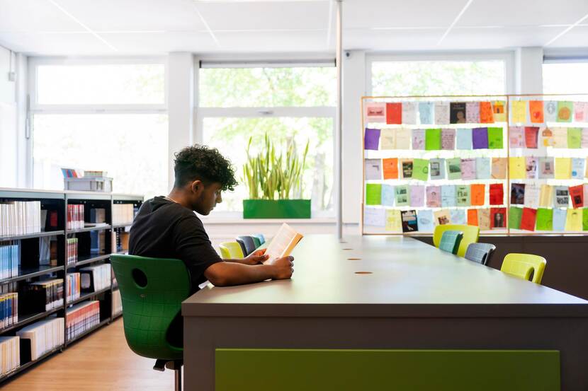 Een jongen leest een boek in de schoolmediatheek