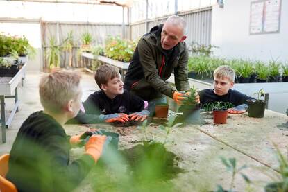 Drie leerlingen verpotten planten met een leraar
